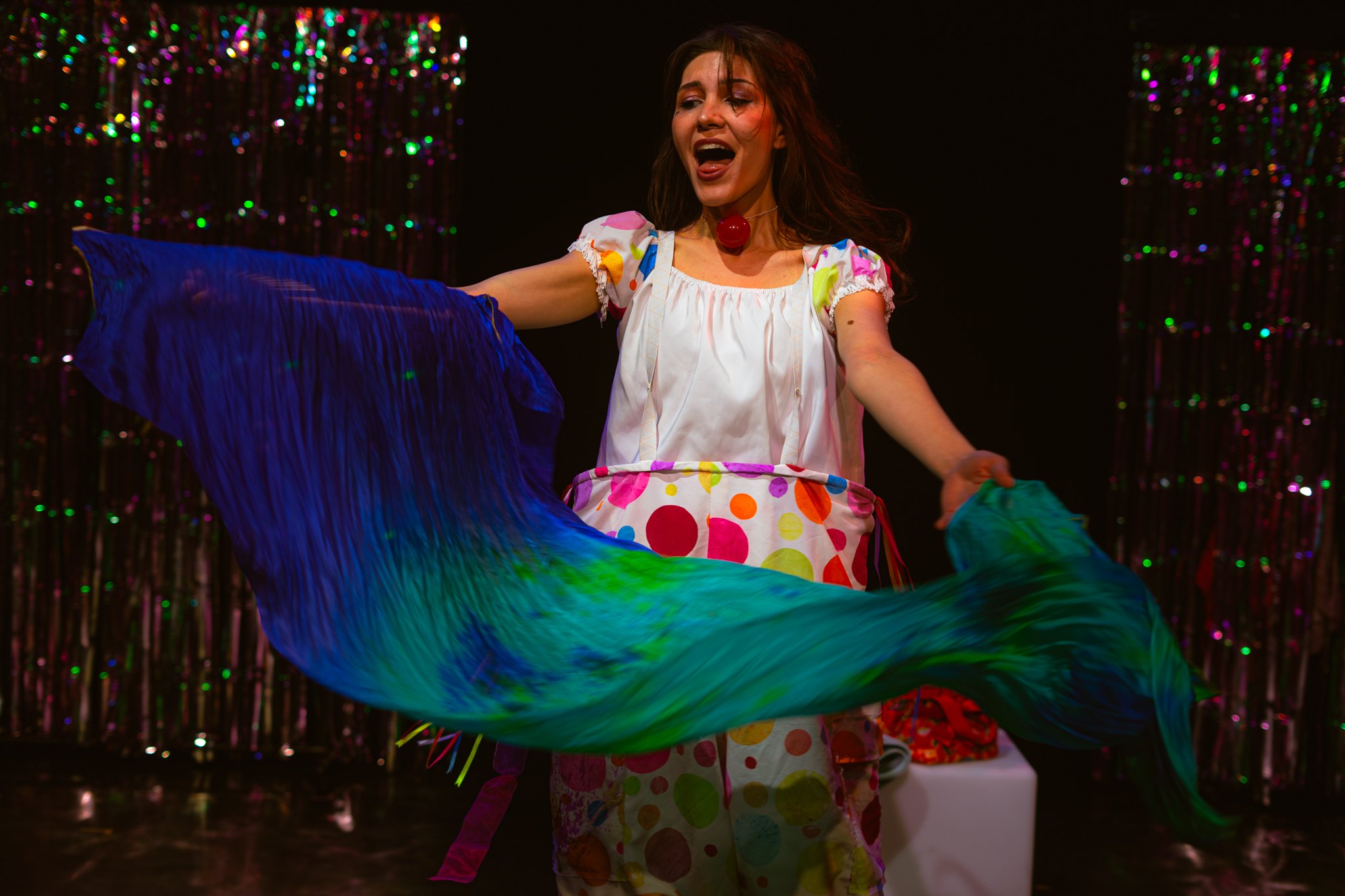 Feride Morçay as Dahlia sweeping a blue and green silk through the air